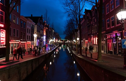 Een gracht in het centrum van Amsterdam bij nacht, met de weerspiegeling van de lichten en mensen die langs de kade wandelen.